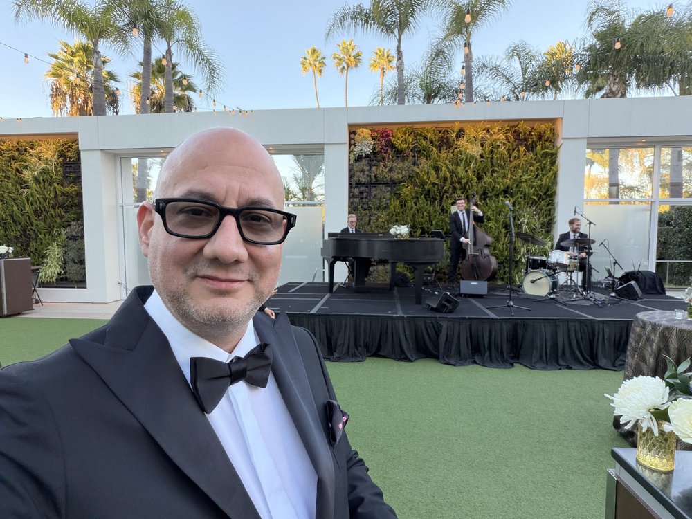 Luis Giraldo in tuxedo at the Beverly Hilton garden with the jazz trio playing on stage behind him